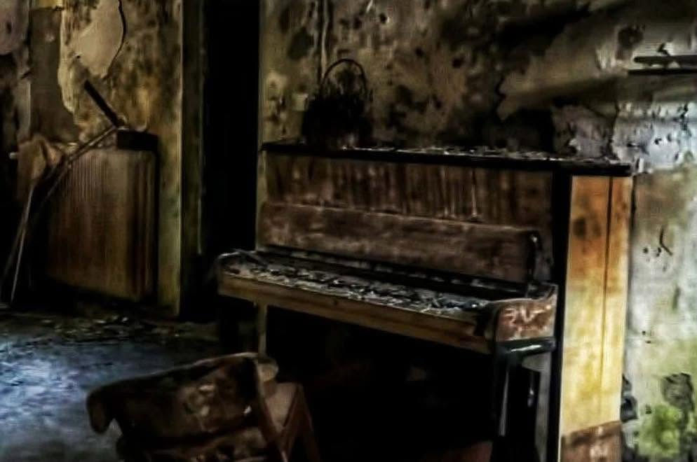 An old piano still standing in a room where the plaster has fallen from the walls