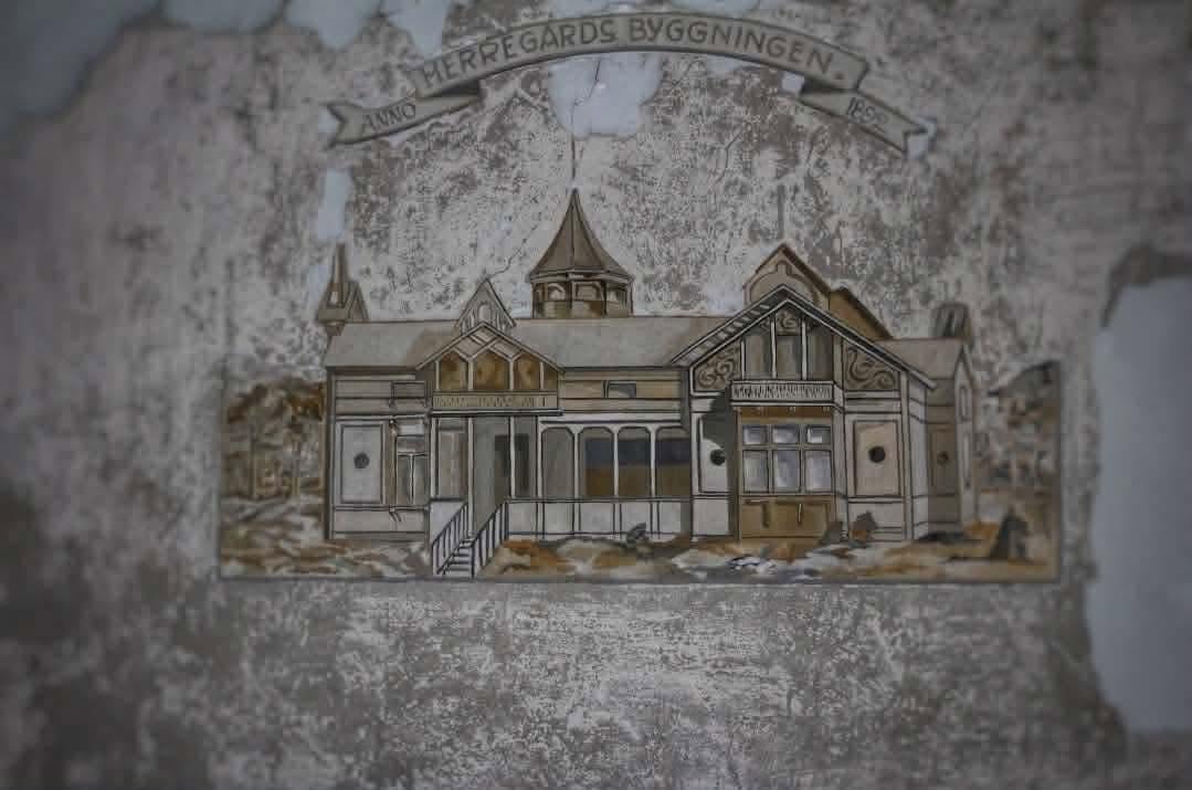 A wall relief reading ANNO HERREGÅRDS BYGGNINGEN 1899, showing the old wooden manor house